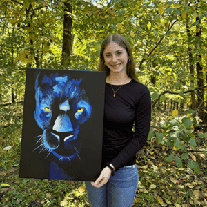 Artist holding blue panther acrylic painting with piercing yellow eyes on stretched canvas, titled ‘On the Prowl’ by Olivia Catherine